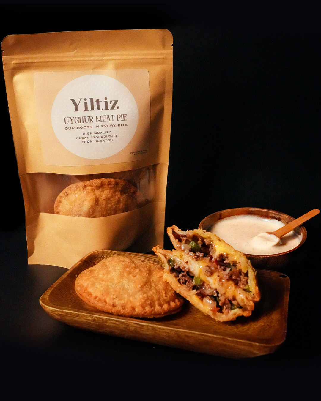 A delicious meat pie package displayed with one whole meat pie, one cut in half showing its filling, and sauce on the side