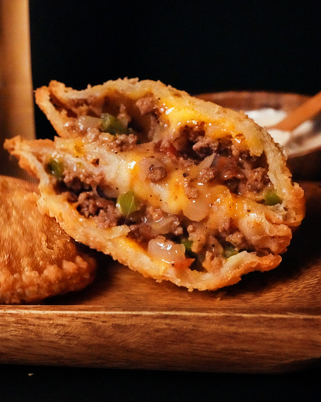 One meat pie cut in half showing its filling, and sauce on the side.
